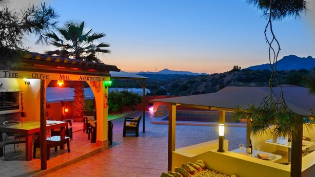 Un área de comedor al aire libre con una pérgola, mesas y sillas, con vistas a un paisaje montañoso.