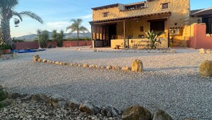 Un edificio de piedra con techo de tejas, un porche cubierto y un patio de grava.