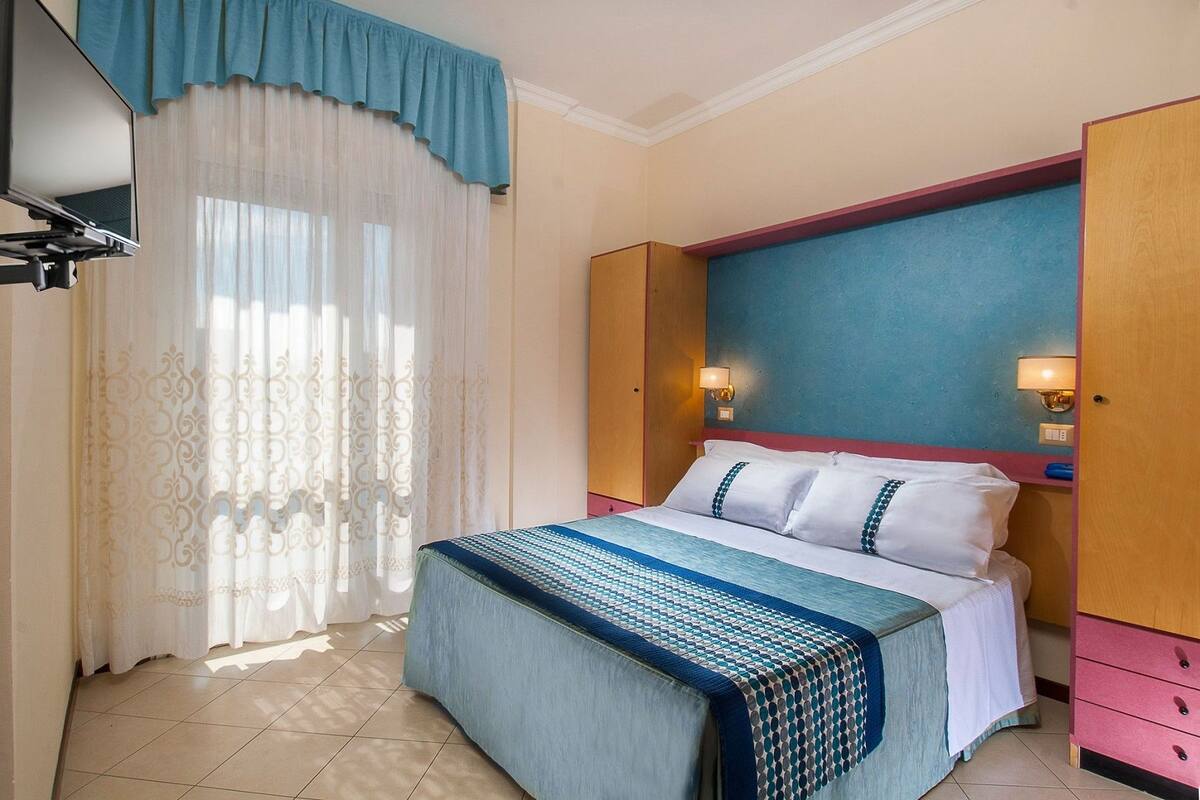 Ein Hotelzimmer mit Bett, Vorhängen, einem Fernseher und einer Wandleuchte.