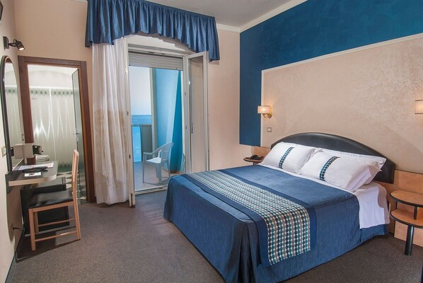 Ein Hotelzimmer mit Bett, Schreibtisch, Stuhl, Nachttisch und einem durchgegangenen Tür sichtbaren Badezimmer.