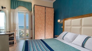 Une chambre d’hôtel avec un lit, un bureau et une vue sur la mer, visible à travers une porte vitrée.