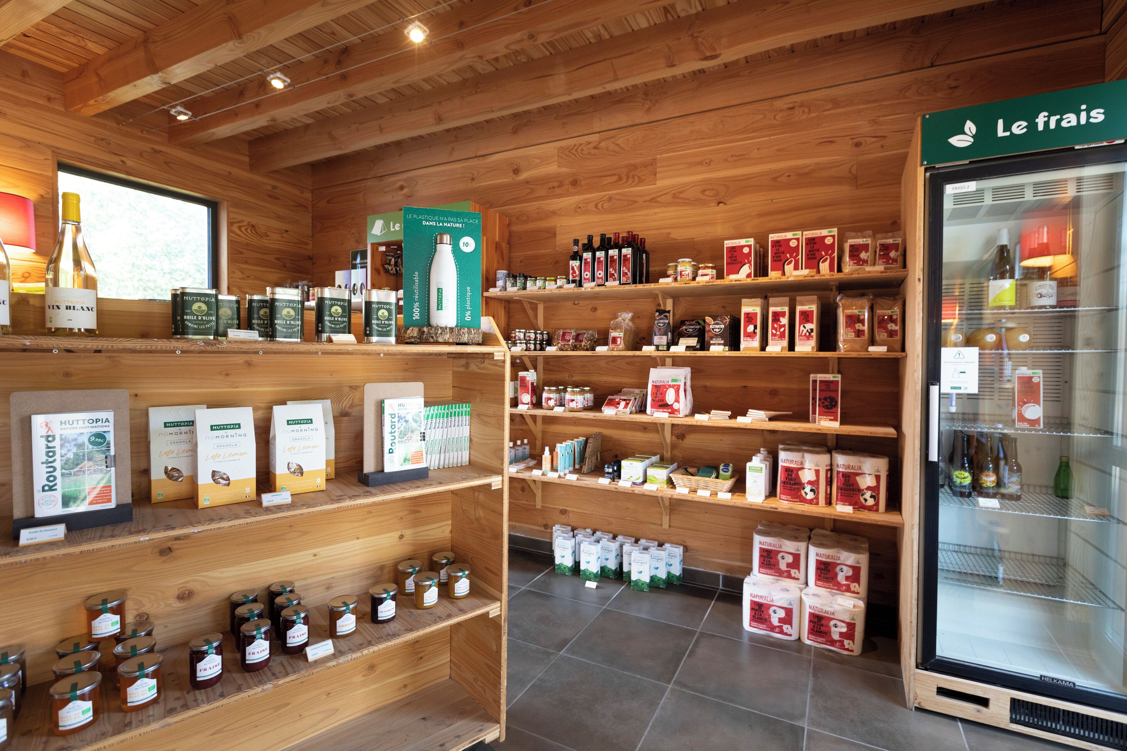 Un intérieur en bois, avec des étagères remplies de divers produits alimentaires, un réfrigérateur-vitrine et une fenêtre laissant entrer la lumière naturelle.