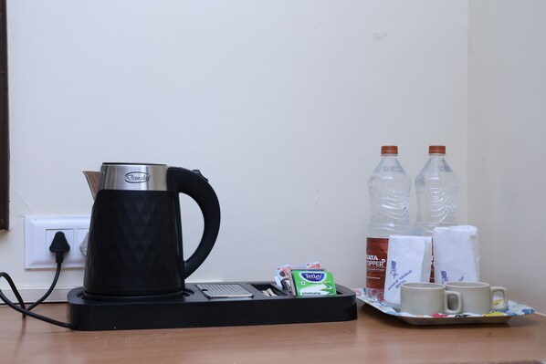 A coffee maker, two bottles of water, a box of tissues, and two cups on a tray. - Gujarat Bhavan Hotel (Karjat)