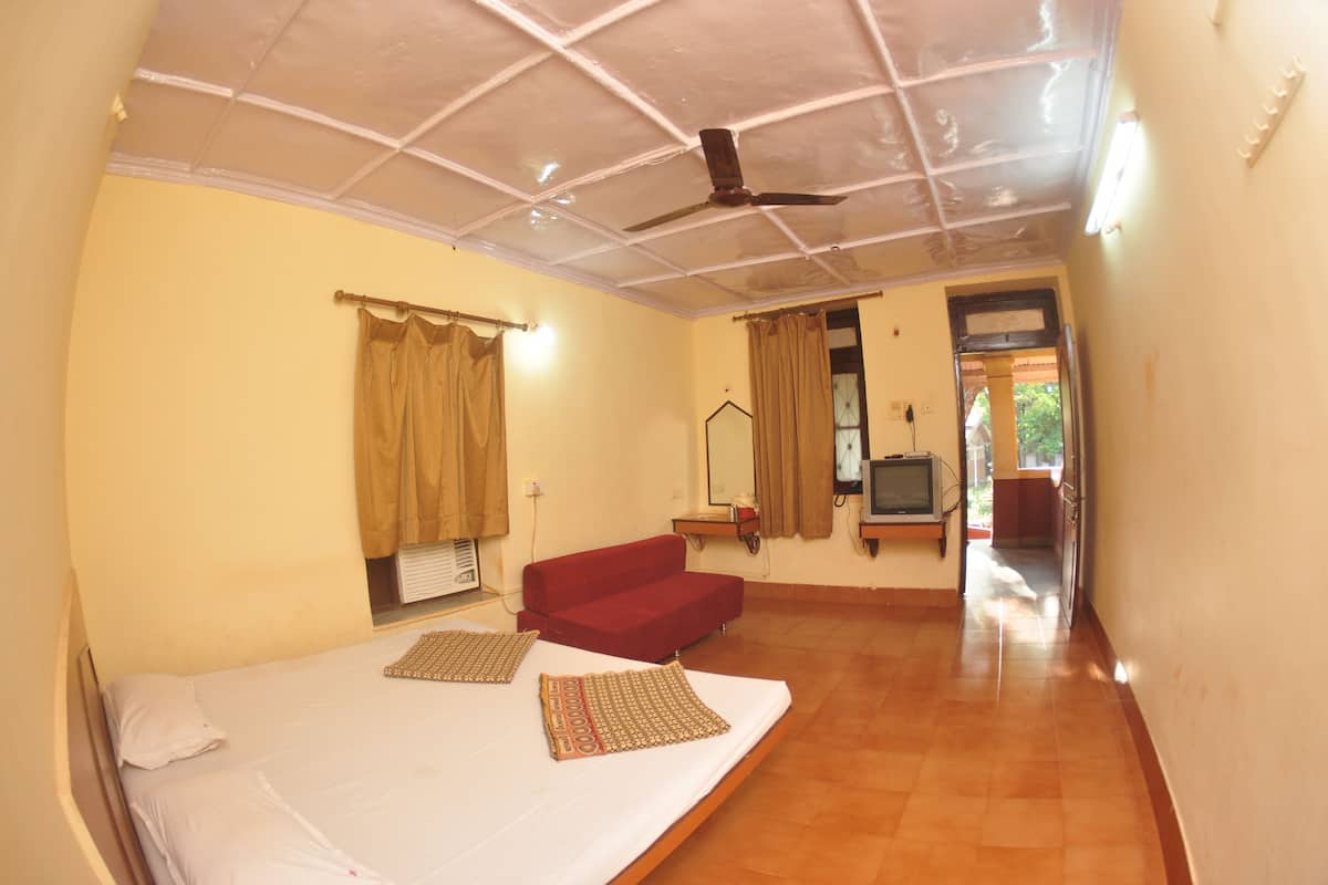 A room with a bed, a red sofa, a ceiling fan, and a television.