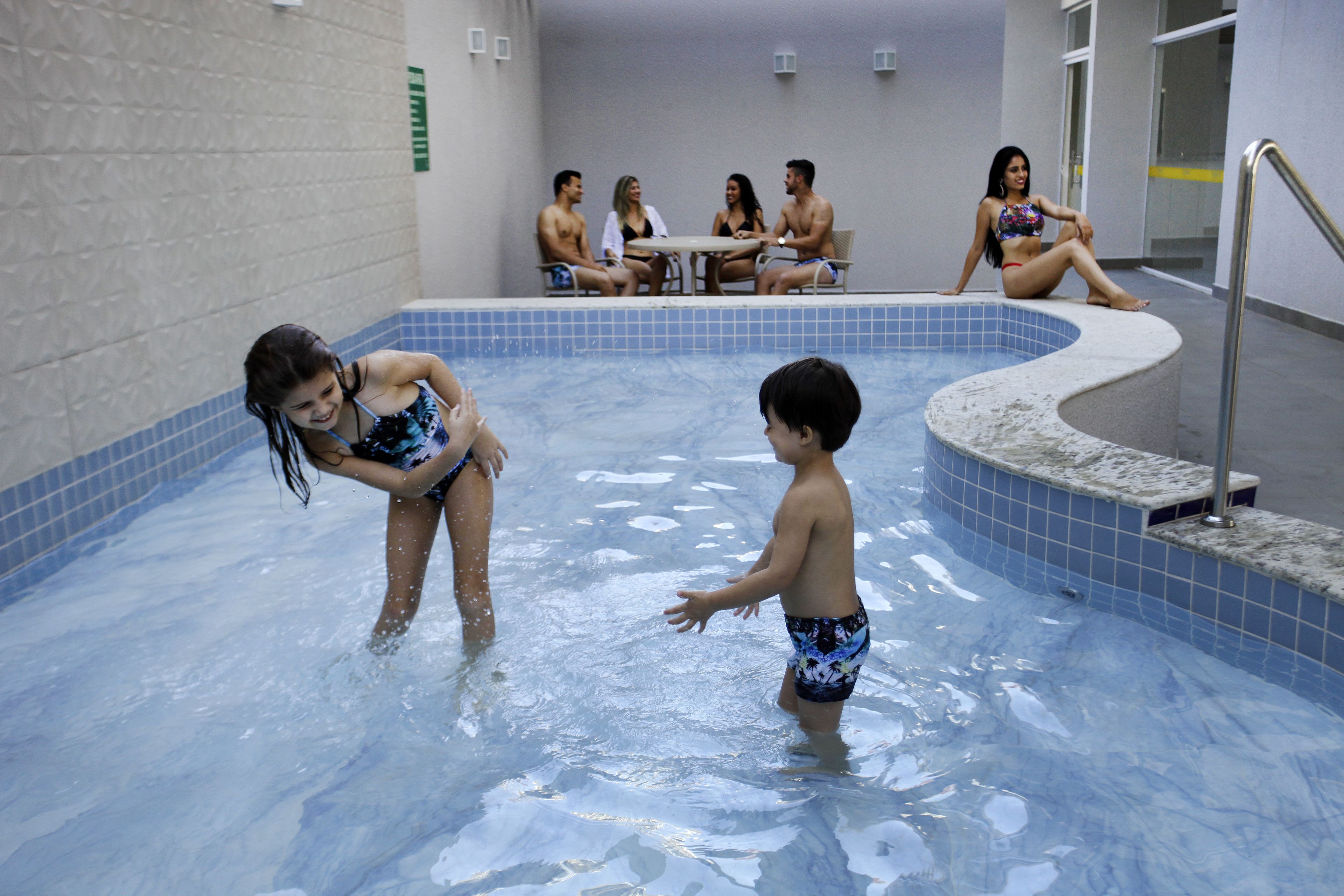 A swimming pool with a tiled interior, a seating area with tables, and a group of people.