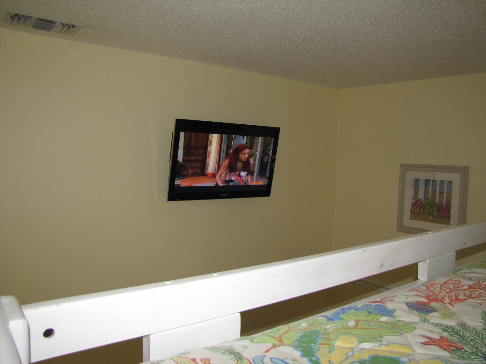 A bedroom with a single bed, a television mounted on the wall, and a framed picture.
