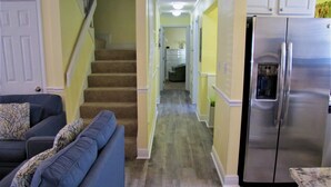 A living room with a blue sofa and patterned pillows, a kitchen with a stainless steel refrigerator, and a wooden staircase leading to another room. - Windancer Cottages by Crystal Waters (Destin)