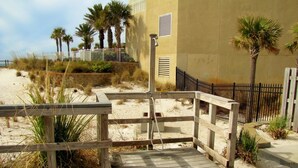 A wooden boardwalk leading to a building with a sandy beach and palm trees in the background. - Windancer Cottages by Crystal Waters (Destin)