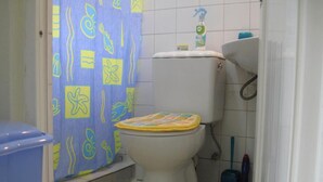 A bathroom with a toilet, a shower curtain, a sink, and a trash bin. - Velvet House (Nairobi)