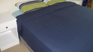 A bed with a blue bedspread and two pillows, a white nightstand with a drawer, and a patterned curtain. - Velvet House (Nairobi)
