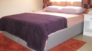 A bed with a purple blanket, a white pillow, and a striped bed skirt. - Velvet House (Nairobi)