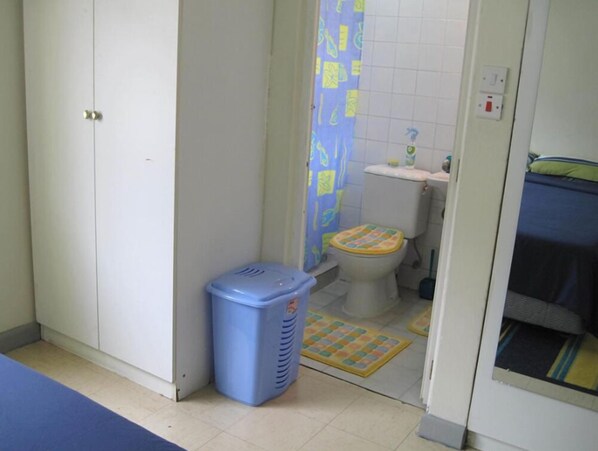 Ein kleines Badezimmer mit Toilette, einem blauen Mülleimer und einer Duschvorhang.