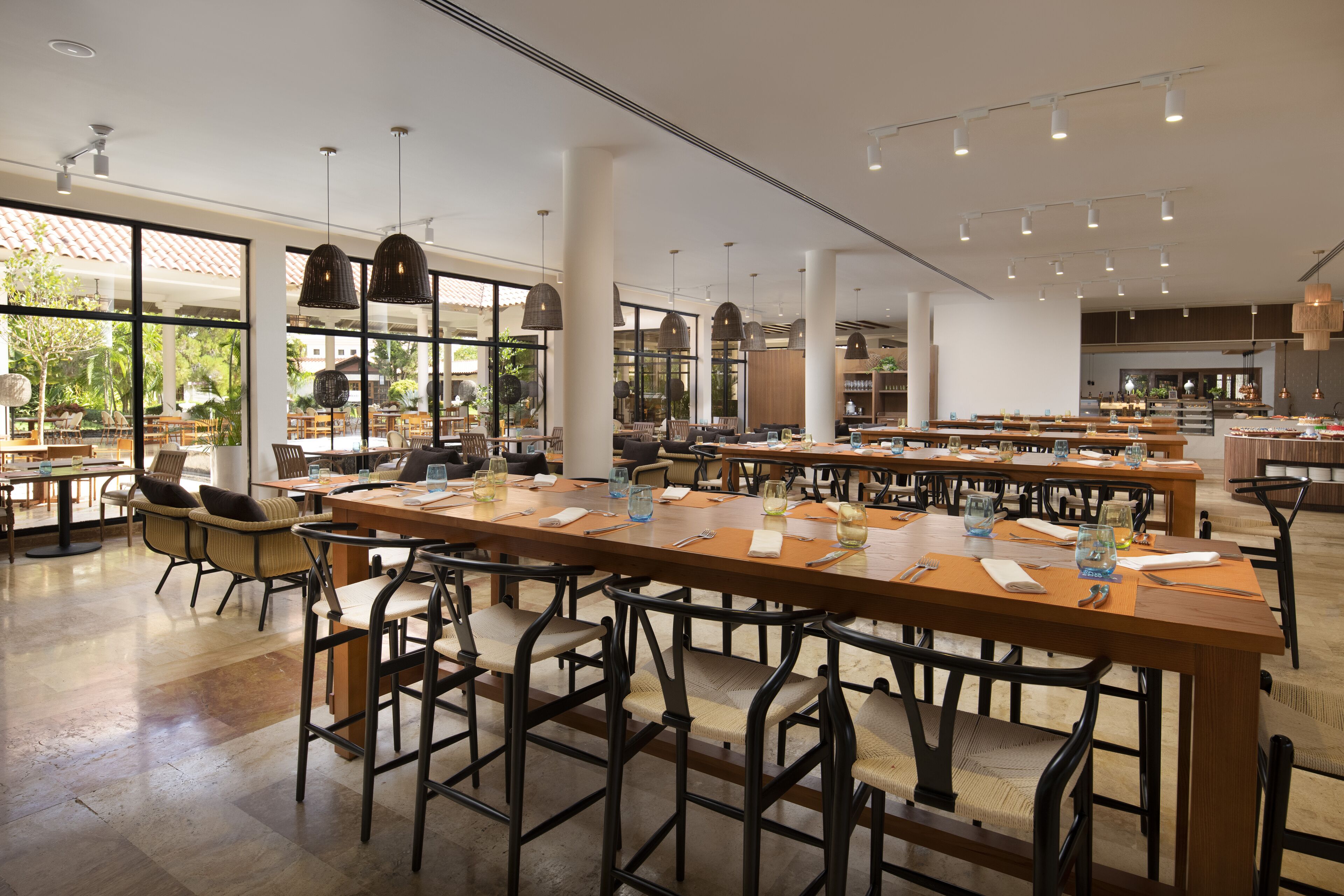 A spacious dining area with long tables and chairs, large windows, and pendant lighting.