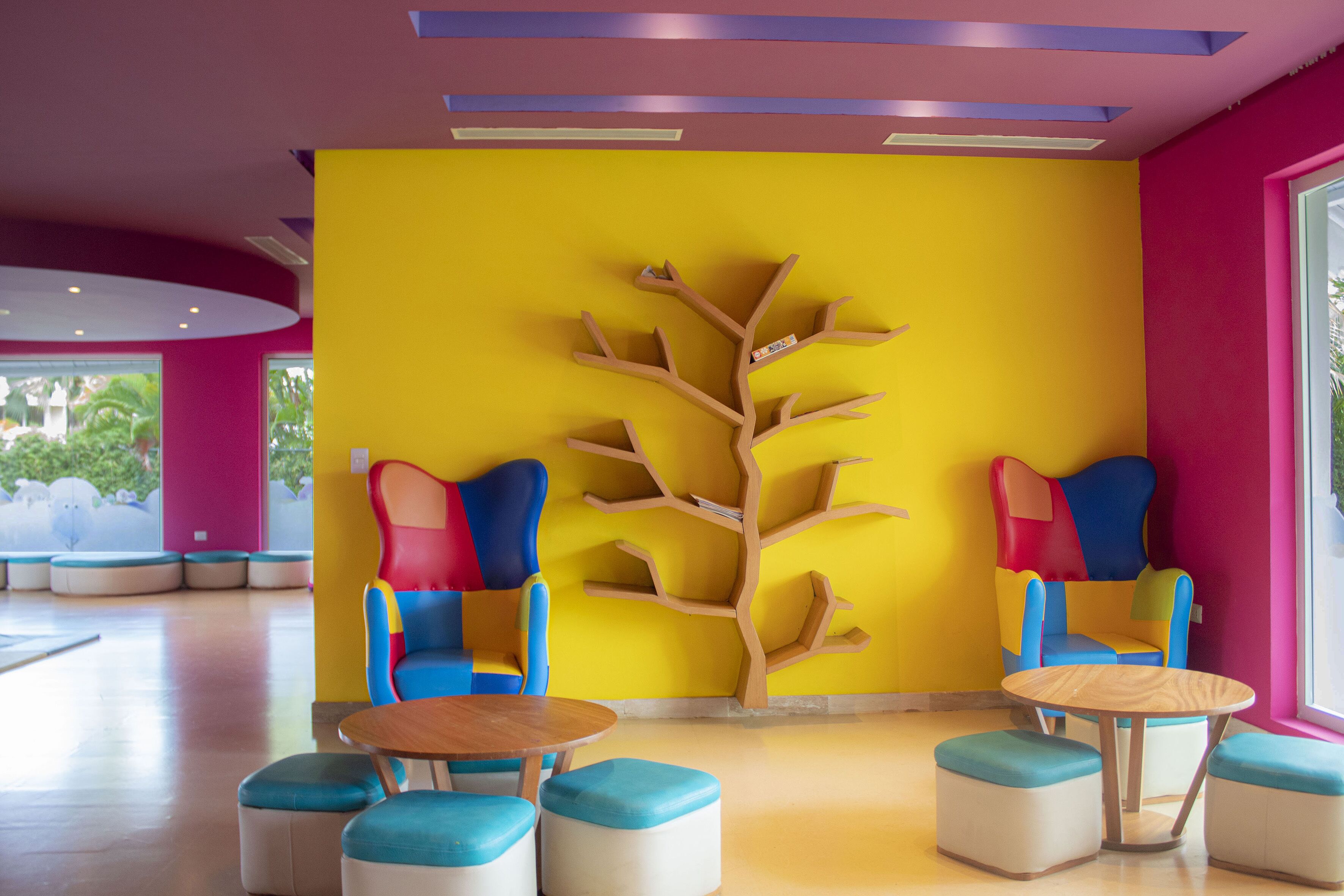 Een vrolijk ingericht interieur met een gele wand, een houten beeld van een boom en kleurrijke zithoeken.