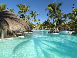 A resort pool with clear water, surrounded by palm trees and thatched-roof structures. - Melia Caribe Beach Resort - All Inclusive (Punta Cana)
