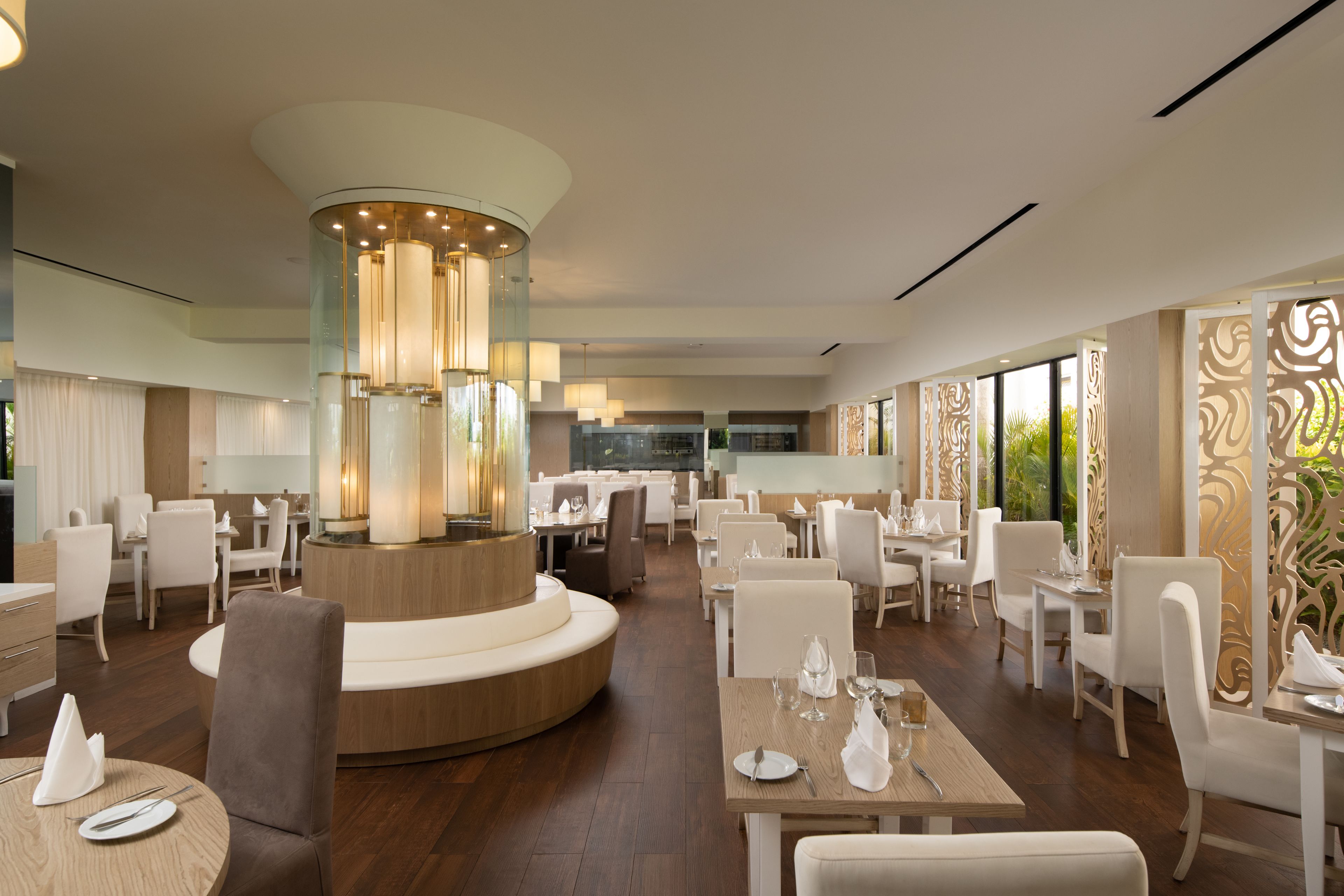 Uma sala de jantar moderna com mesas redondas, cadeiras brancas e um lustre central.