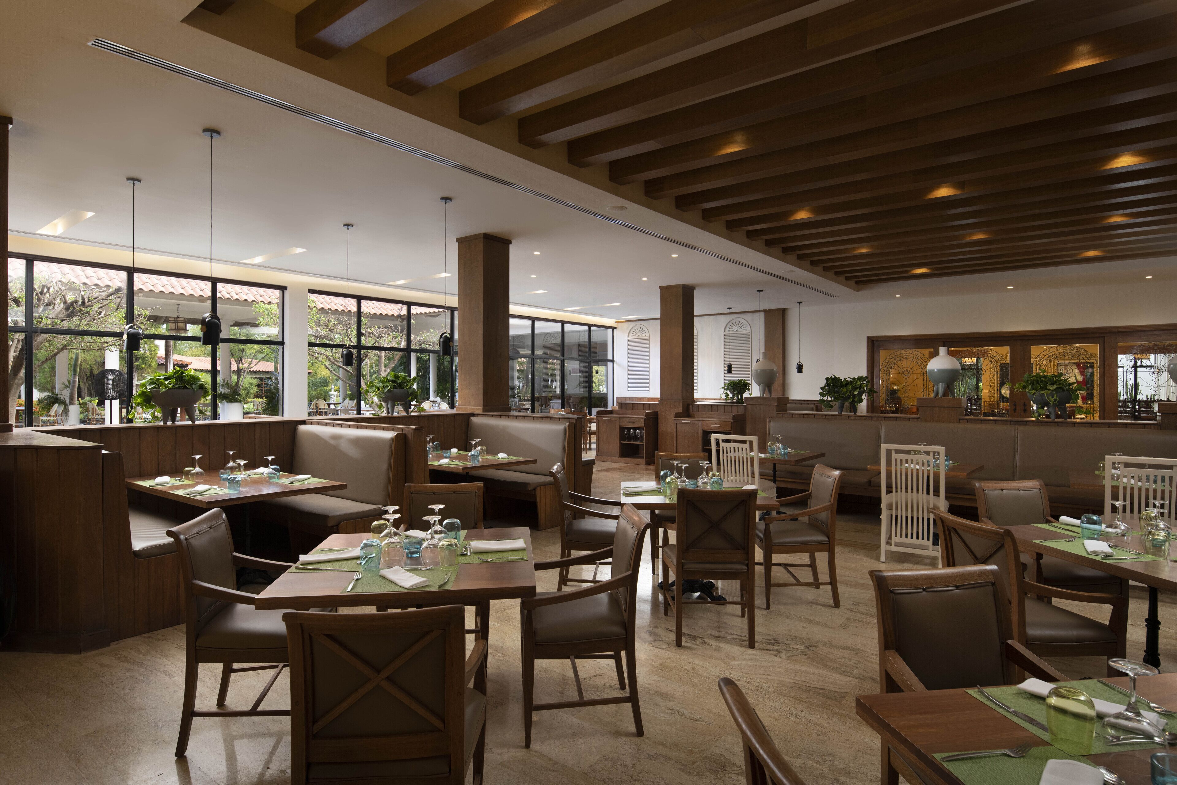 Un restaurant avec des meubles en bois, de grandes fenêtres et des plantes d’intérieur.