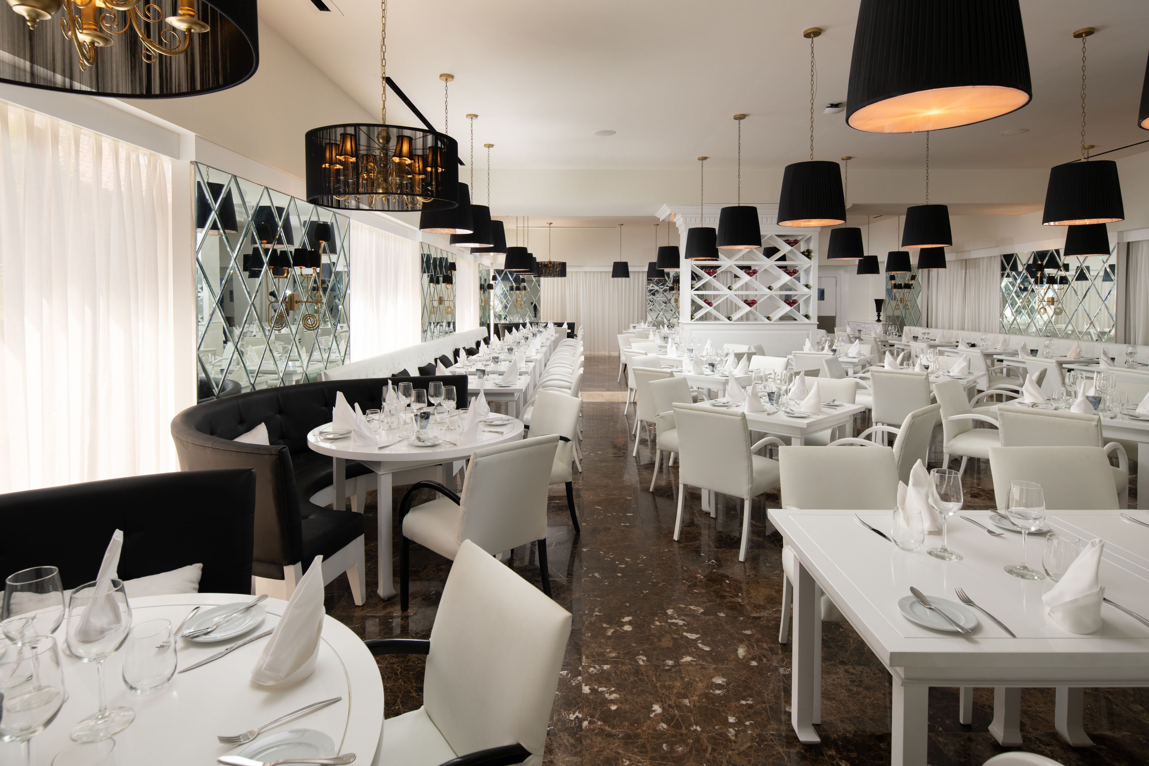 Un restaurant avec des tables et des chaises blanches, des suspensions noires et un sol en marbre.