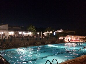 Una piscina con gente nadando, rodeada de edificios y zonas de estar al aire libre.