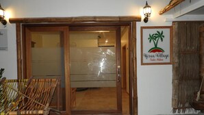 Une porte en bois avec un panneau de verre, une enseigne indiquant « Karara Village Thoddo-Maldives », et une chaise en osier à l’extérieur.