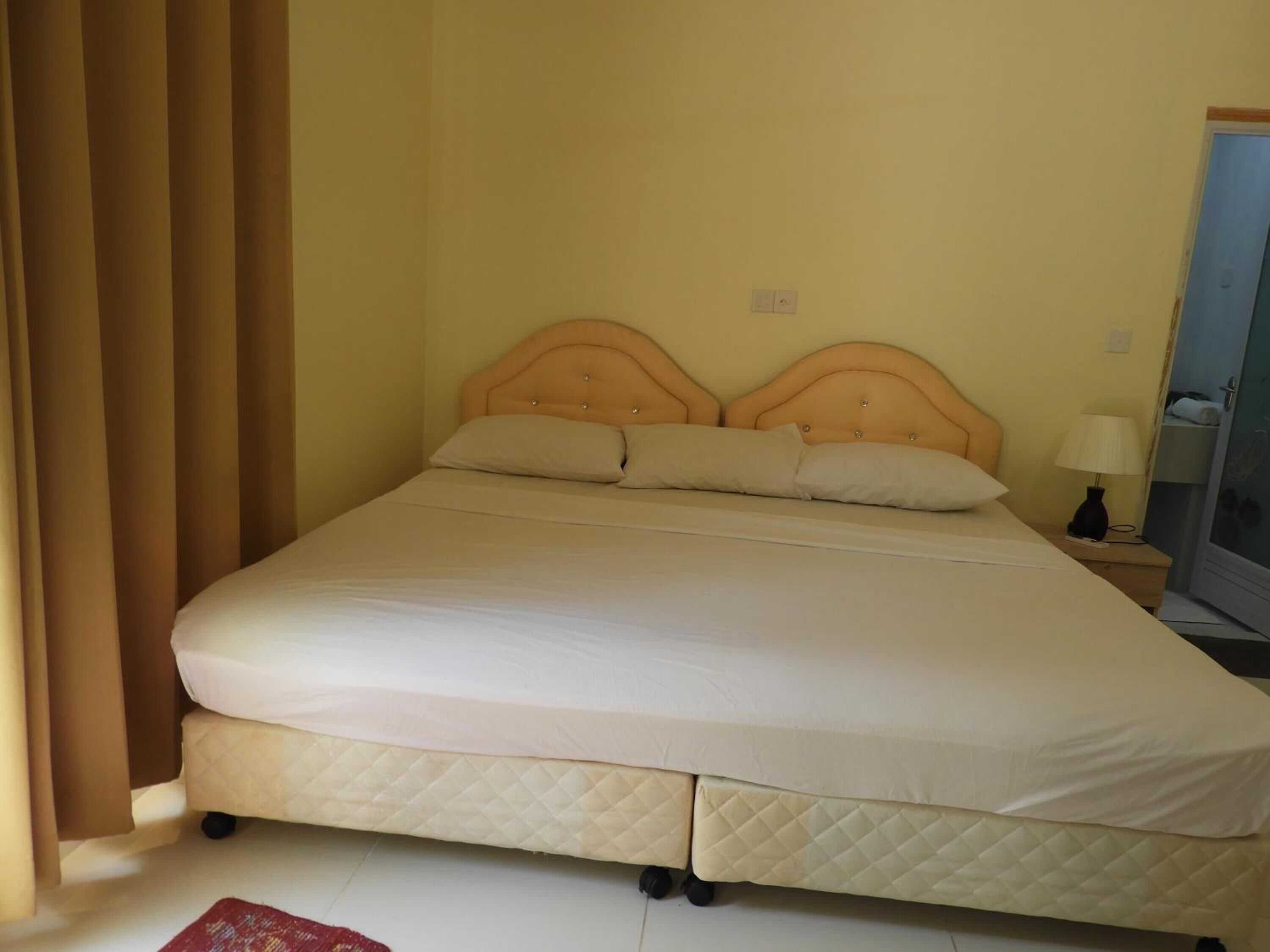 Una cama con cabecera, una mesita de noche con lámpara y un espejo en la pared.