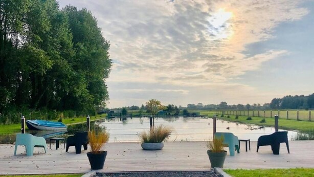 Une terrasse au bord du lac, dotée de sièges et de jardinières, entourée d’arbres et offrant une vue sur le lac.