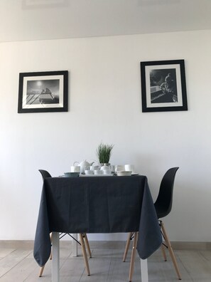 Et spiseområde med et bord dækket til to personer, indrammede fotografier på væggen og en potteplante på bordet.