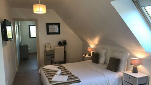 Une chambre avec un grand lit, un bureau et une chaise. Il y a une fenêtre sur le côté droit de la pièce.