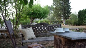 A wooden bench with a cushion, a small table with a cup and saucer, and a book with glasses on a metal chair. - Casa Rural Aire (Muro del Alcoy)