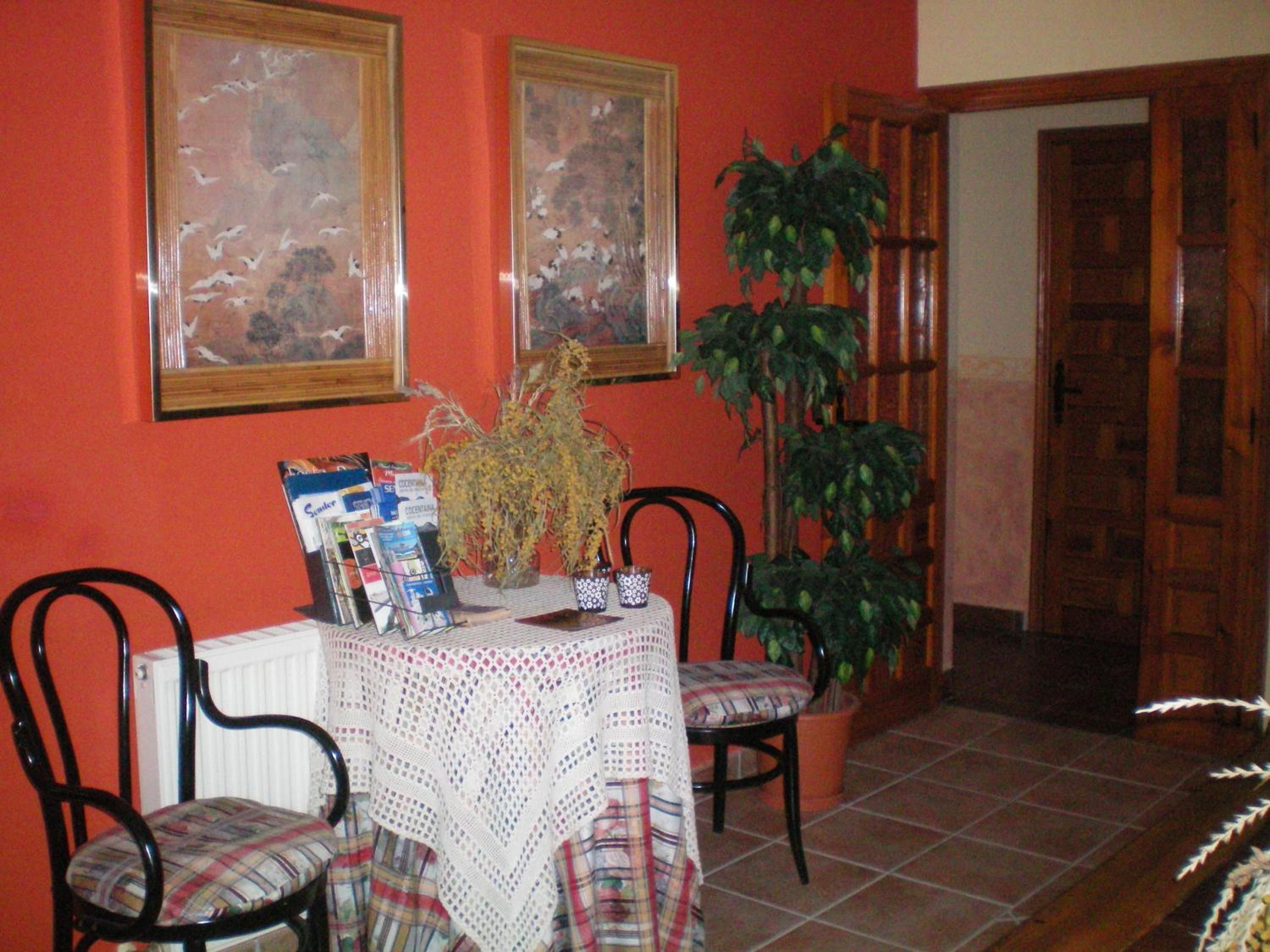 A dining area with a table, chairs, a potted plant, and framed artwork on the wall.
