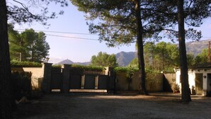 A gated area with a gravel path, trees, and a mountain in the background. - Casa Rural Aire (Muro del Alcoy)