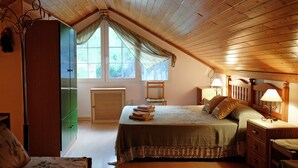 A cozy bedroom with a sloped ceiling, a bed with a green bedspread, a wooden wardrobe, and a window with a view of trees. - Casa Rural Aire (Muro del Alcoy)