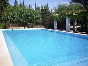 A rectangular swimming pool with clear blue water, surrounded by trees and a pergola structure.