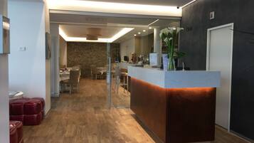 A modern reception area with a wooden floor, a reception desk, and a dining area in the background.