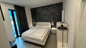 A modern bedroom with a large bed, a dark accent wall, and a view of the outdoors through a window. - Athos Hotel (Riva del Garda)