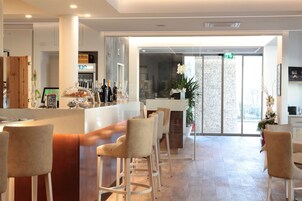 Un área de bar moderna con una barra alargada, taburetes acolchados y un expositor de vidrio.