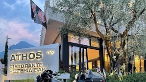 A motorcycle parked in front of a building with a sign that reads "ATHOS RISTORANTE PIZZERIA BAR." - Athos Hotel (Riva del Garda)