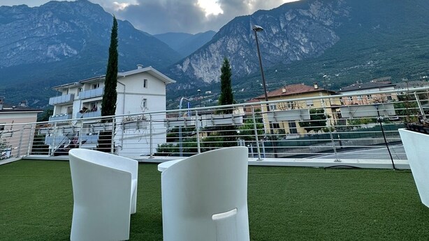 A rooftop terrace with two white chairs, a view of a mountain range, and a clear sky. - Athos Hotel (Riva del Garda)