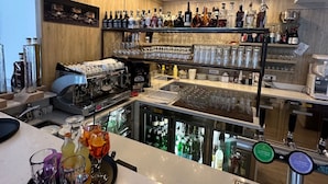 A bar area with a counter, shelves of bottles, glasses, and a coffee machine. - Athos Hotel (Riva del Garda)