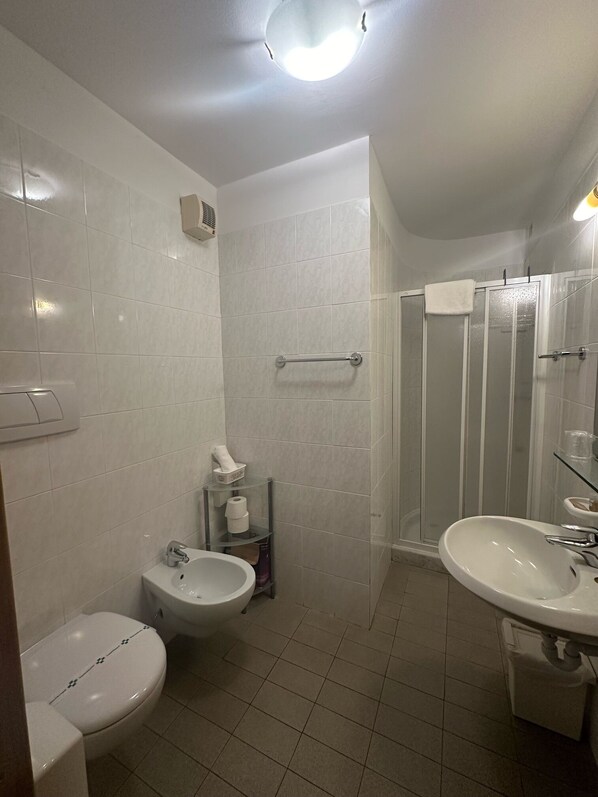 Un baño con inodoro, bidé, lavamanos y cabina de ducha de vidrio.