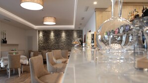 A modern bar area with a long counter, bar stools, and a variety of bottles. - Athos Hotel (Riva del Garda)