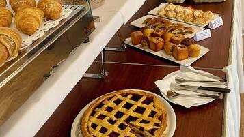 A buffet with various baked goods and desserts, including pastries, pies, and a cake.
