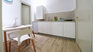 A small kitchen with white cabinets, a wooden dining table with a white chair, and a clock on the wall. - Apartments Top Central 2 (Belgrade)