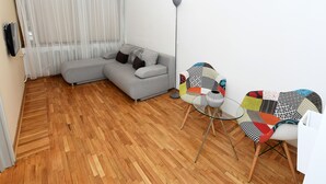 A modern living room with a grey sectional sofa, a glass coffee table, and patterned chairs. - Apartments Top Central 2 (Belgrade)