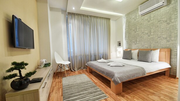 A modern bedroom with a bed, bedside table, TV, and a decorative bonsai tree. - Apartments Top Central 2 (Belgrade)