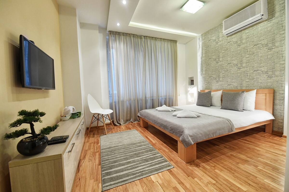 Un dormitorio moderno con cama, mesita de noche, televisor y un bonsái decorativo.