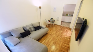 A living room with a grey sofa, a floor lamp, a small table with chairs, and a kitchen in the background. - Apartments Top Central 2 (Belgrade)