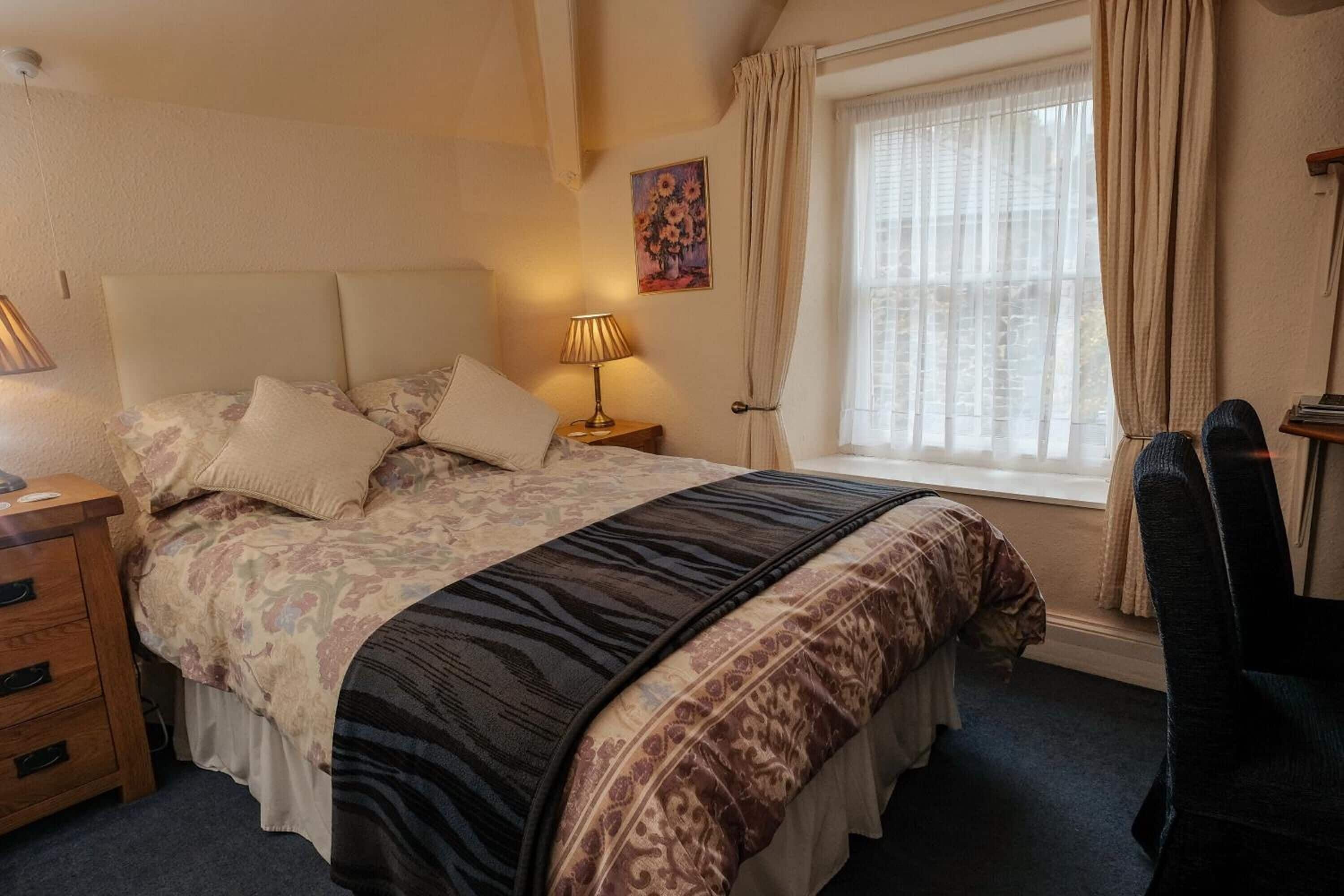 A bedroom with a bed, nightstands, a chair, a window with curtains, and a painting on the wall.
