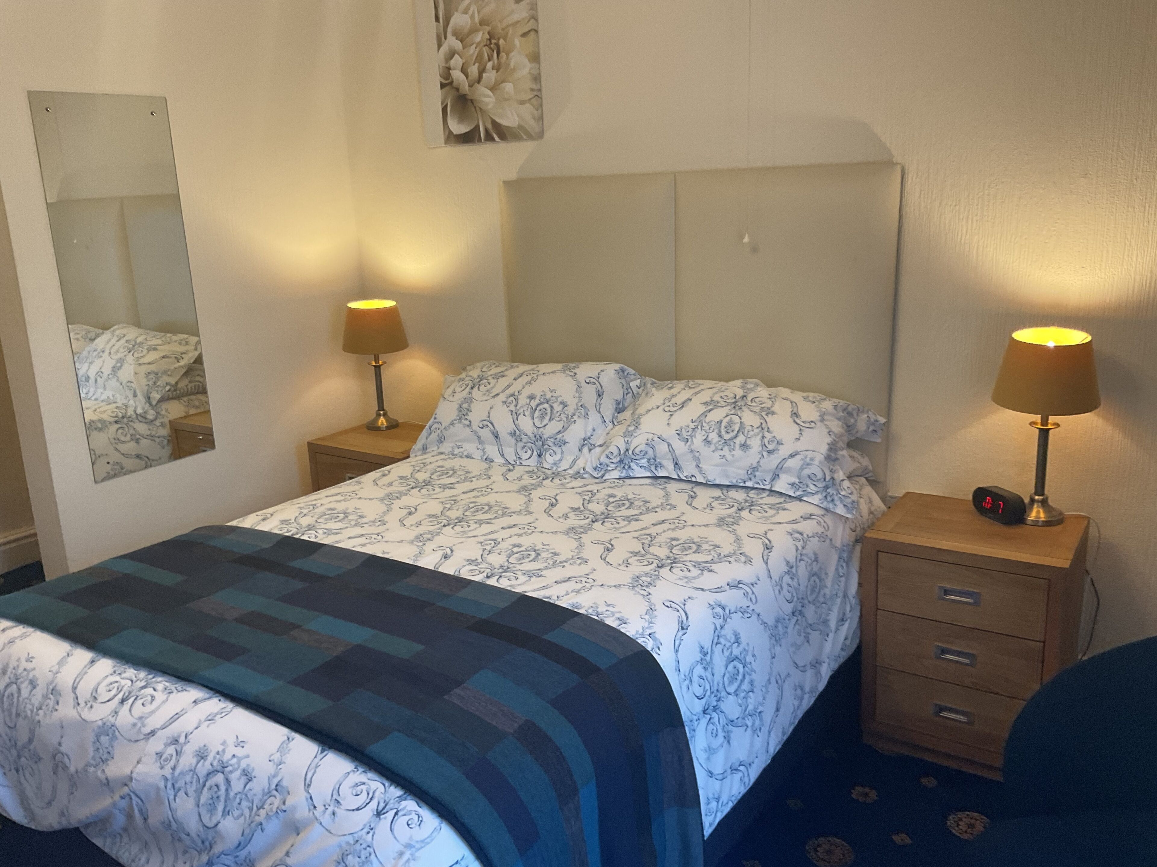A hotel room with a bed, two bedside tables with lamps, a mirror, and a wall-mounted artwork.