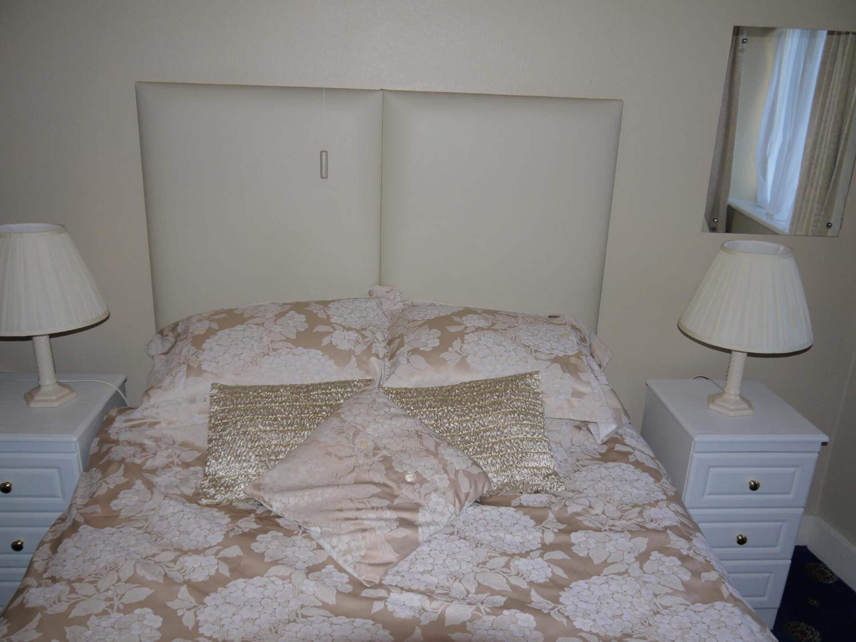 Una cama bien hecha con ropa de cama floral, dos lámparas de noche y un espejo en la pared.